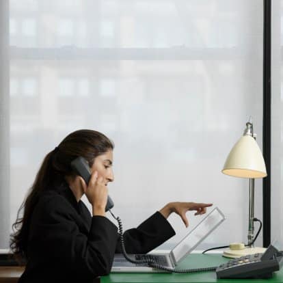businesswoman using laptop and telephone indoors